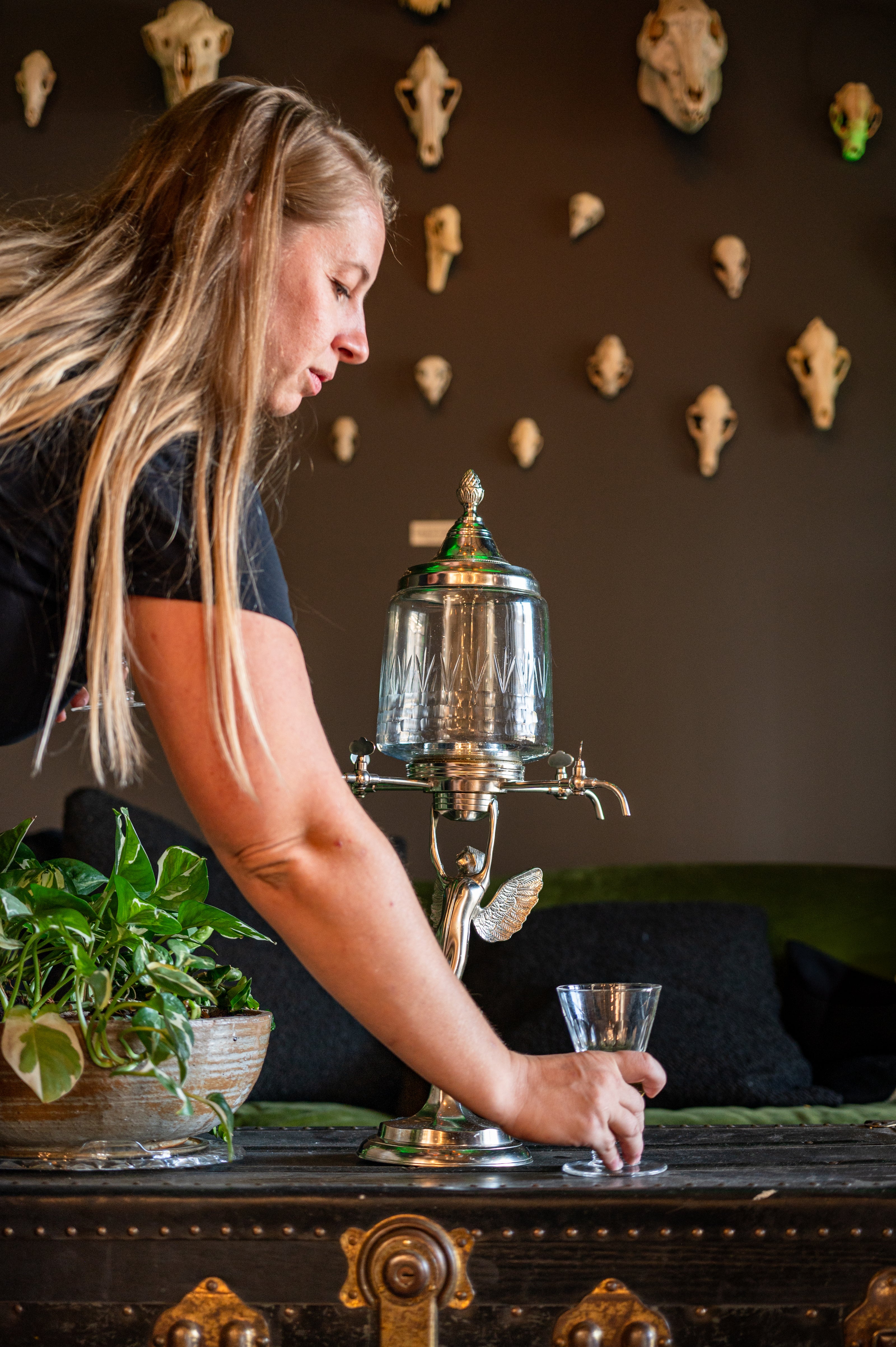 woman with long blonde hair placing a glass under an absinthe dripper