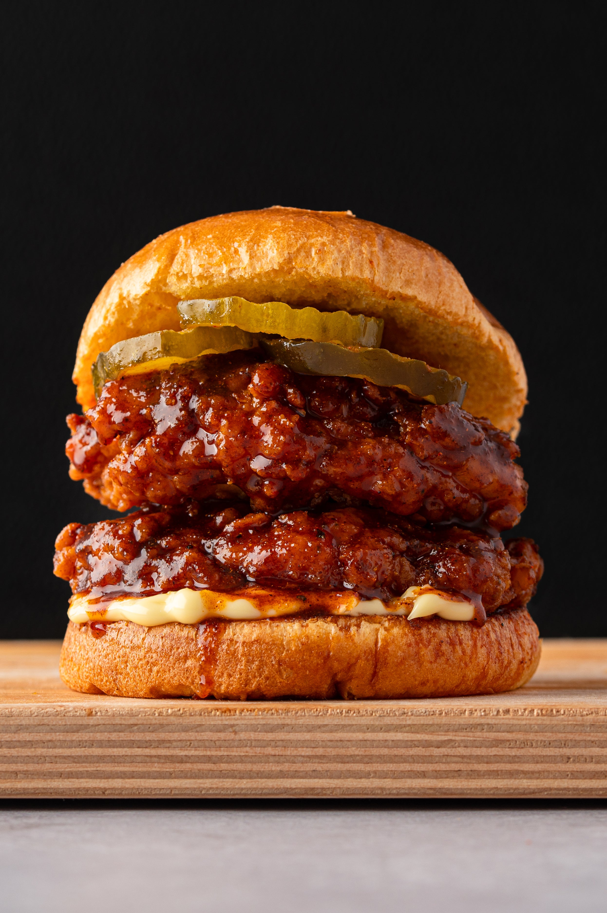 Double layered Nashville Hot Chicken Sandwich with pickles and mayo on a wooden board