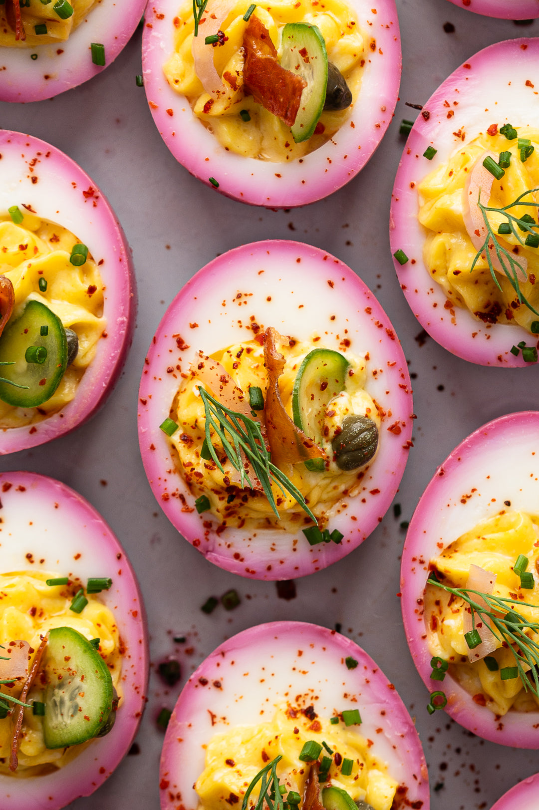 Flatlay of pink deviled eggs with capers, dill, chives, and crispy prosciutto.