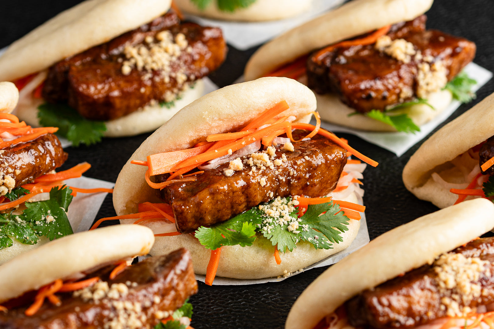 Bao buns with meat, carrots, and greens on a black surface
